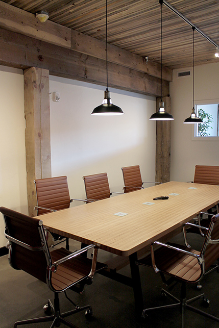 The conference room featuring un-touched exposed beams, wooden plank ceiling, and black metallic light fixtures